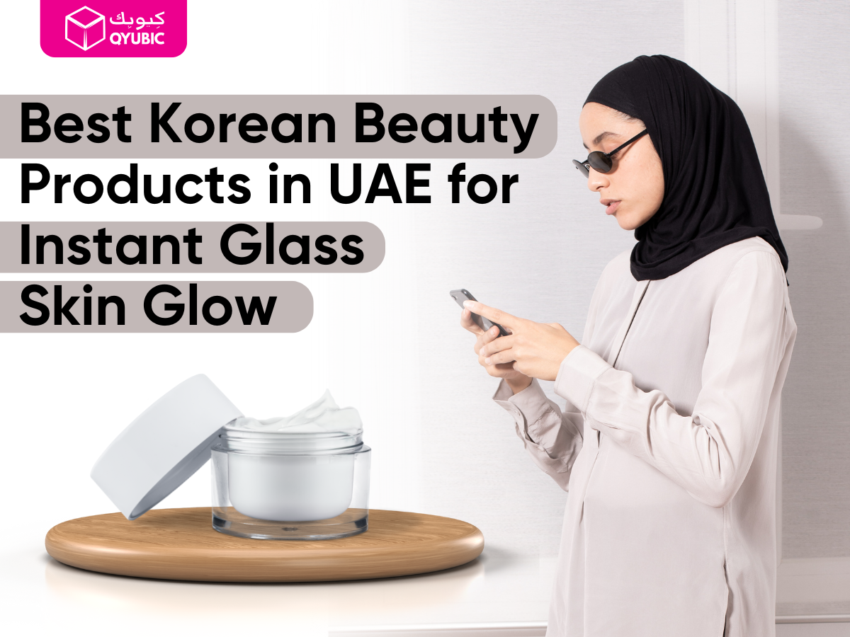 A Muslim woman in a hijab uses her phone while standing indoors, next to a cosmetic jar on a wooden platform. The image promotes “Best Korean Beauty Products in UAE for Instant Glass Skin Glow” by QYUBIC, a discount and coupon platform.