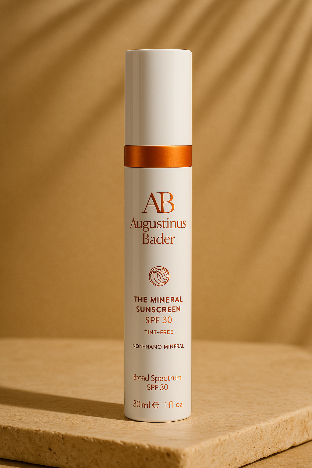 Tall, sleek white bottle of Augustinus Bader The Mineral Sunscreen SPF 30, labeled as tint-free and non-nano mineral, standing on a stone-textured platform with soft shadows in the background.